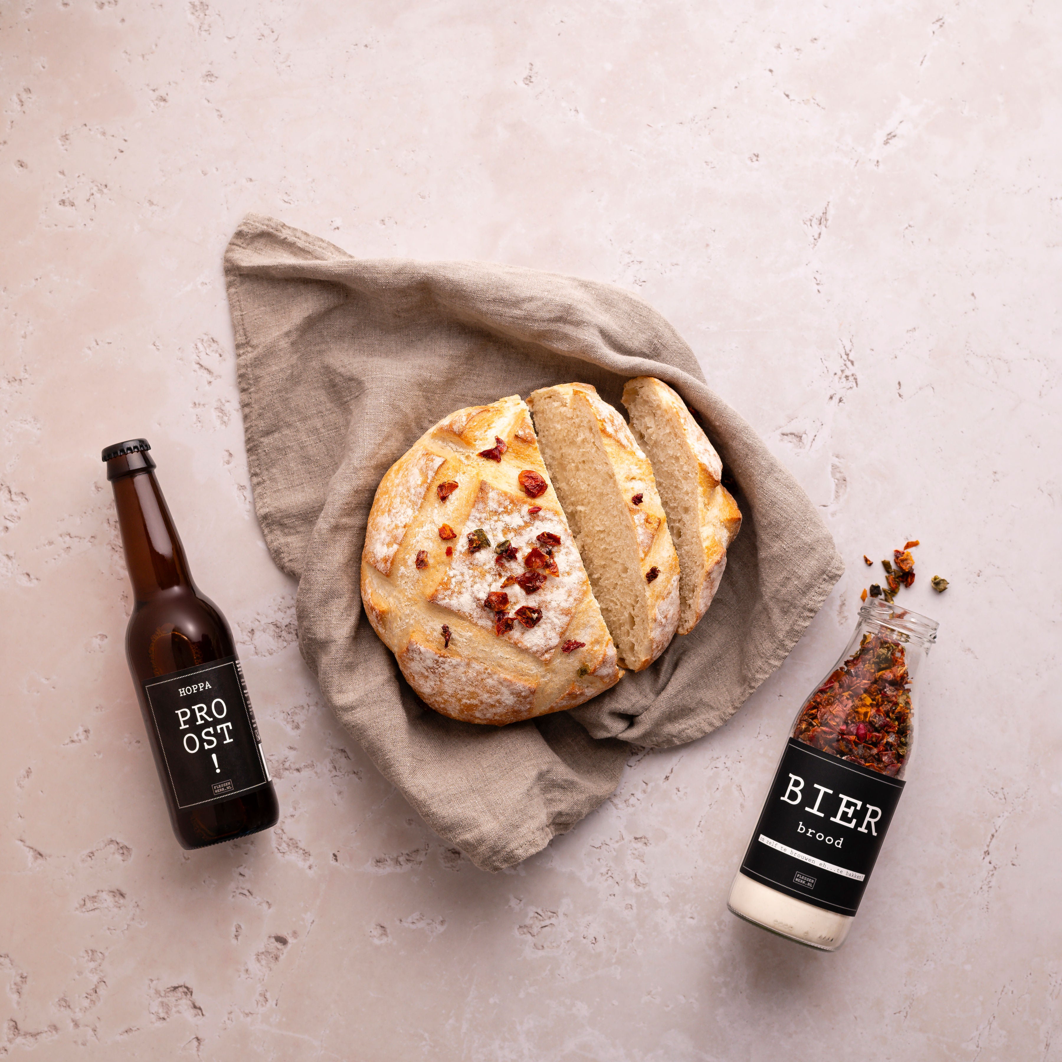 Een glazen fles met de etiket 'bierbrood', gevuld met ingrediënten om een eigen bierbrood te maken en het eindresultaat van een heerlijk brood. Hiernaast ligt het biertje wat erin gegaan is