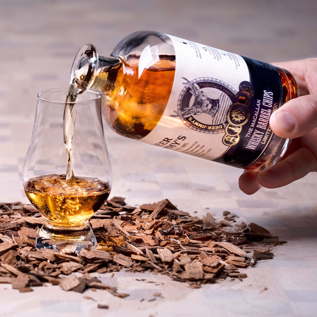 Een fles whisky wat ingeschonken word in een glas en staat op houtsnippers