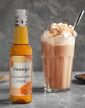 doorzichtige kunststof flesje met karamel toffee siroop naast een groot glas met koffie en slagroom