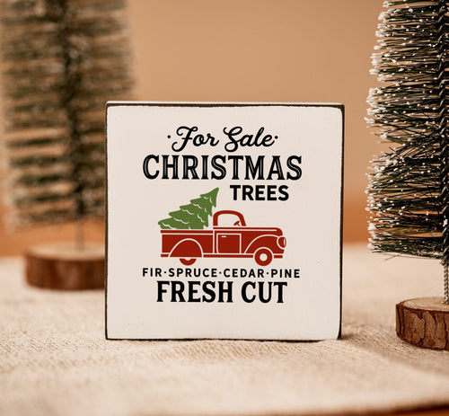 wit houten blok met een rode auto en kerstboom afgebeeld en de tekst for sale Christmas trees